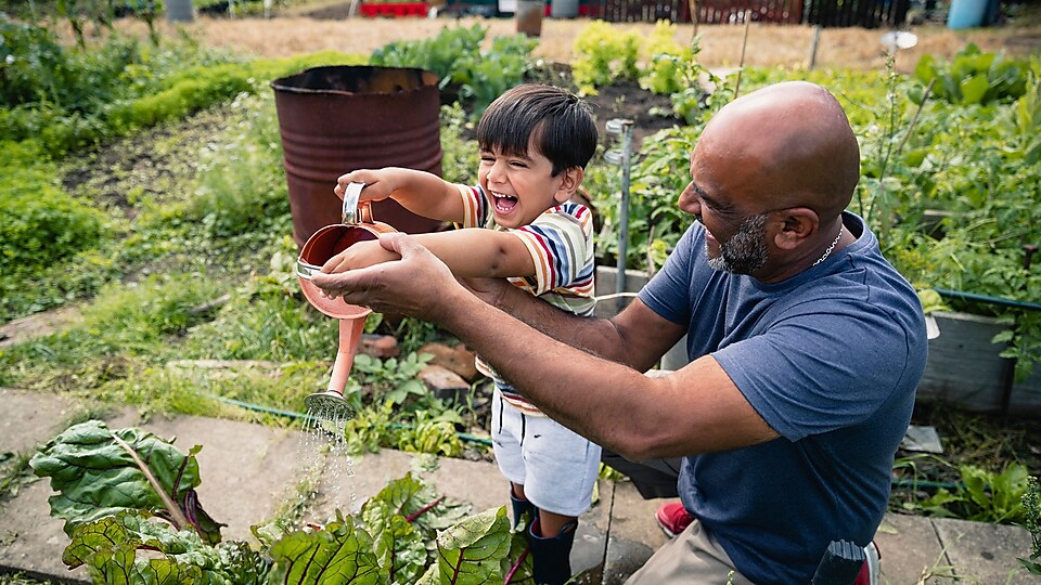 Người đàn ông đang giúp một đứa trẻ tươi cười tưới cây trong vườn