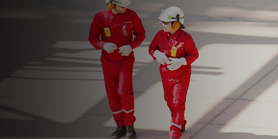 Nam và nữ công nhân mặc áo trang phục màu đỏ, đội mũ bảo hiểm trắng và đeo thiết bị bảo vệ thính giác khi đi bộ